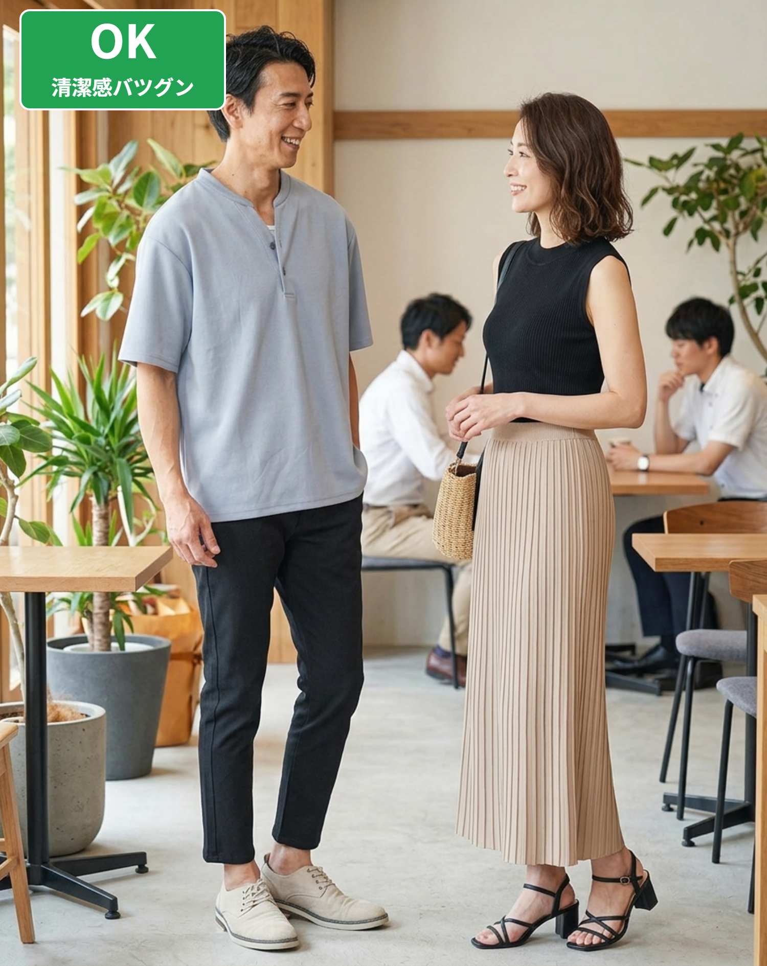 OKコーデ　待ち合わせ場所でのサックスブルーオーバーサイズヘンリーネックTシャツと黒スキニーテーパードアンクルチノパンツの立ち姿シチュエーション（OKマーク付き）