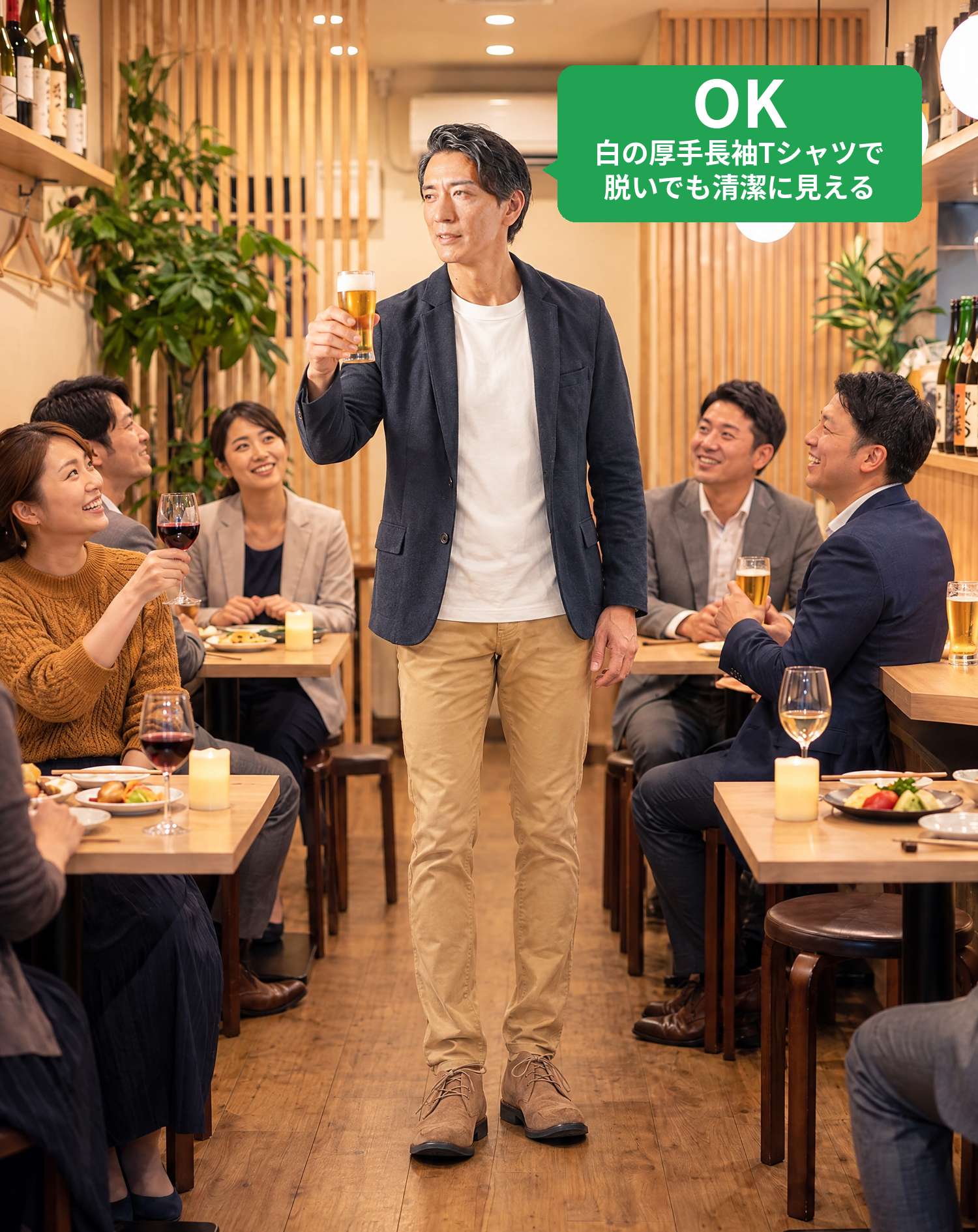 OKコーデ　おしゃれな居酒屋で、ネイビーのジャケットに白の長袖Tシャツを着た男性がビールグラスを掲げて乾杯し、テーブルの仲間が笑顔で見上げるシーン（OKマーク付き）