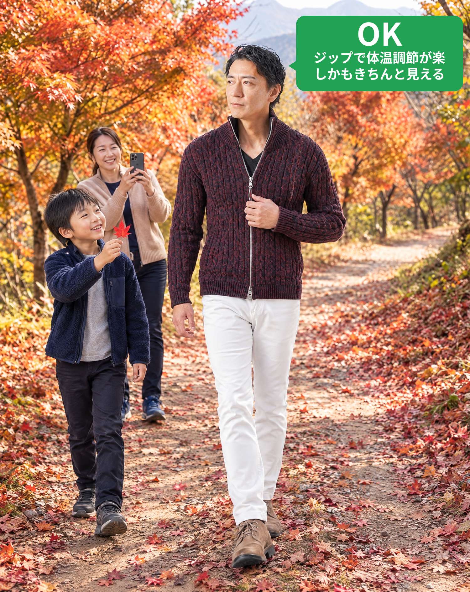 OKコーデ　紅葉の山道をワインのジップアップニットアウター姿で歩き、息子がもみじの葉を見せ、ママがスマホで撮影する家族の秋の旅行シーン（OKマーク付き）