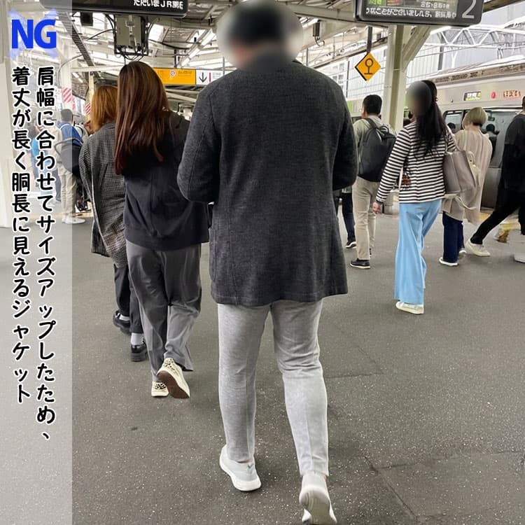 肩幅に合わせてサイズアップしたため、着丈が長く胴長に見えるジャケットを着たガッチリ体型男性例